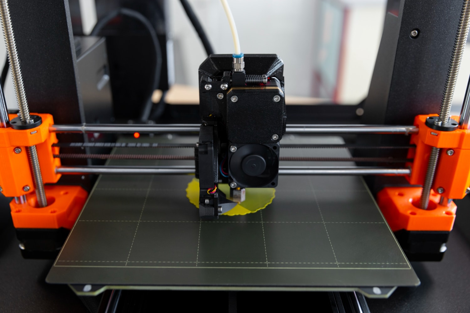 Desktop filament printer depositing yellow plastic on a build plate
